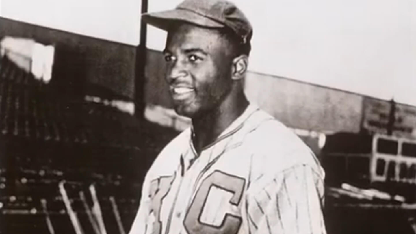 Jackie Robinson, in uniform, smiling in black and white