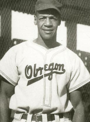 Vintage photo of a baseball player wearing a uniform with Oregon written on it. The player is standing outdoors, wearing a cap, and posing in front of a blurred background, possibly a fence.