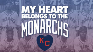 A group of baseball players in vintage Monarchs uniforms pose together. The text reads, My Heart Belongs to the Monarchs with a heart symbol below displaying KC. The image has a blue and red color scheme.