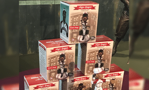 Boxes of baseball-themed collectibles are stacked in a pyramid. Each box features a figure of a player in uniform with Negro Leagues branding. A statue is partially visible in the background.
