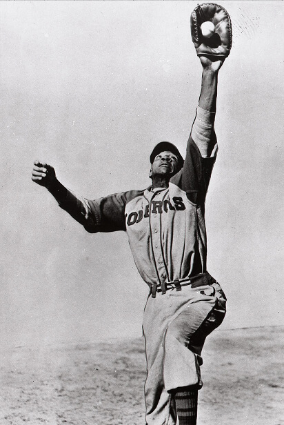 A baseball player, wearing a Dodgers uniform, leaps high with an extended arm to catch a ball in his glove. The black and white photo captures the action and athleticism of the player against a clear sky.