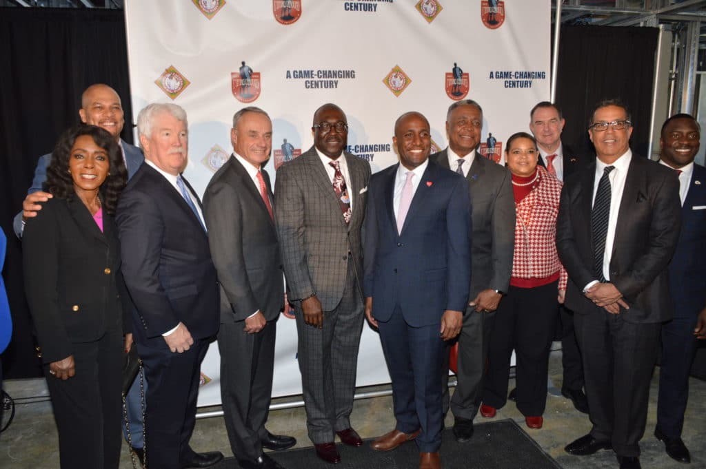 A group of eleven people dressed in formal attire stands together, smiling, in front of a banner with logos and the text A Game-Changing Century at an event.