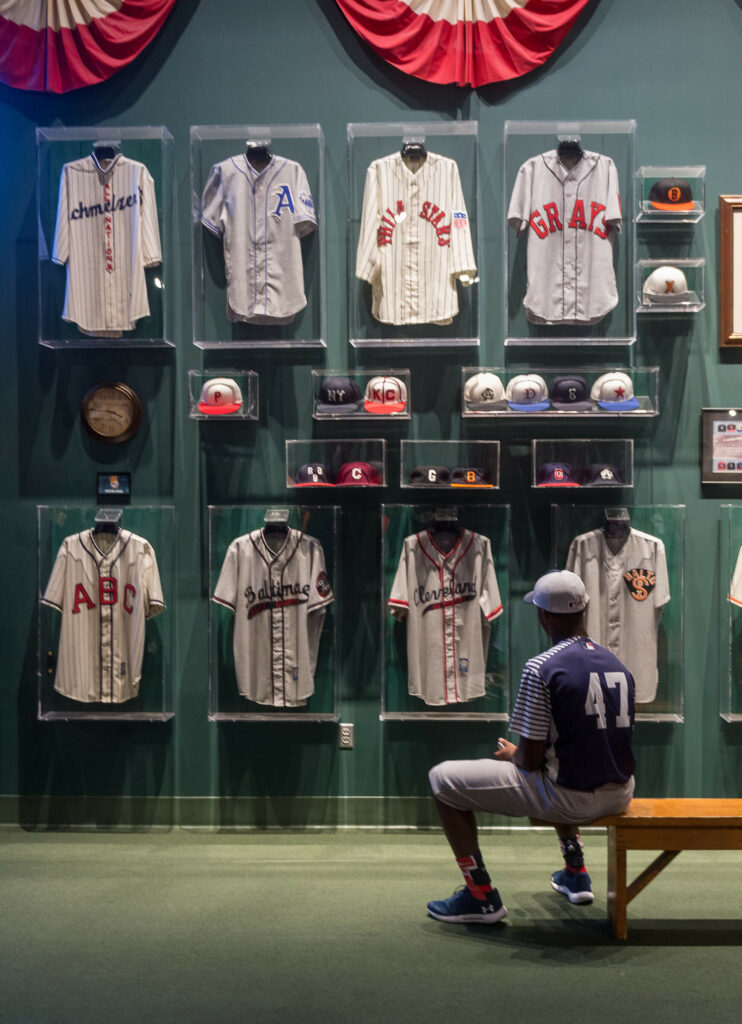 A boy sitting on a bench in the field of legends in the NLBM looking up at the historical jerseys